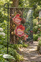 Pink and red cannonball tree flowers and round fruit before a receding rainforest printed on a flat rectangular garden flag