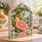 Grapefruit wooden block with pink cut fruit, whole grapefruit, glossy green leaves and cream botanical edging in a bright kitchen.