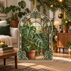 Monstera Greenhouse Christmas Ornament with split Monstera leaves before a receding greenhouse arch and botanical framing