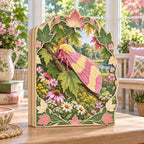 Rosy maple moth wooden block 3 layer with pink and yellow wings, maple leaves and wildflowers in a botanical cottage setting.
